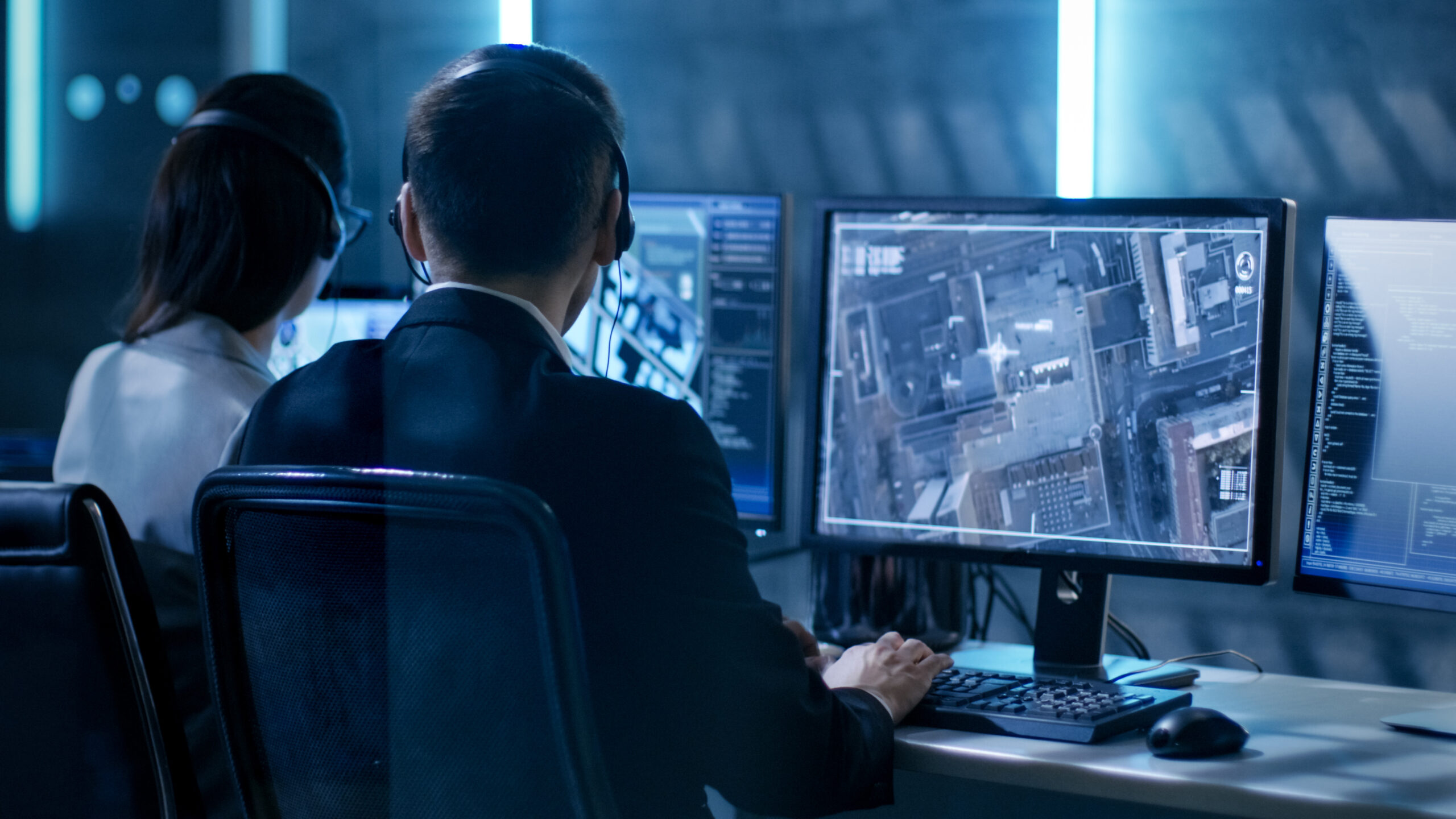 Government Agent Is Tracking Fugitive With Her Computer In Big Monitoring Room Full Of Computers With Animated Screens.